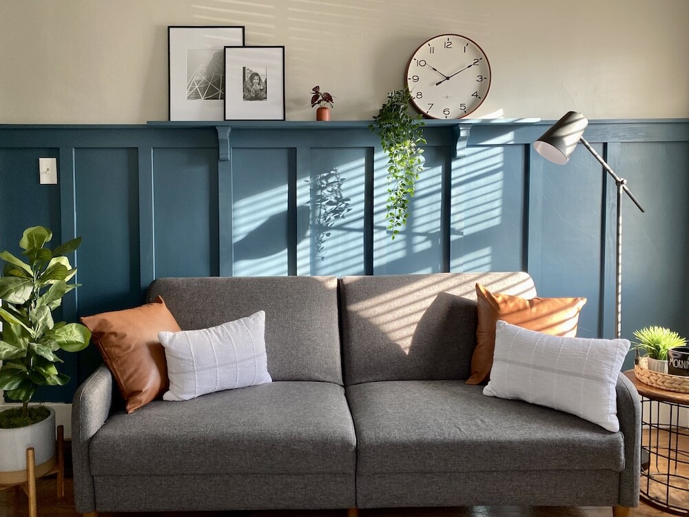 salon z niebieską boazerią i szarą kanapą  niebieska boazeria na ścianie za kanapą
