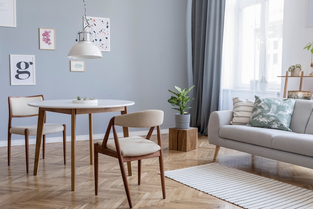 aranżacje salonu z jadalnią z szarą kanapą i okrągłym stołem z drewnianymi nogami 