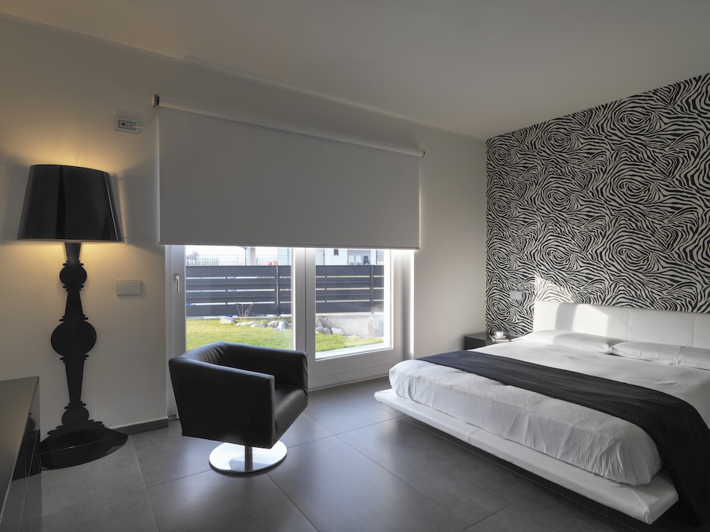 sypialnia z tapetą w czarno-białe wzory za zagłówkiem  sypialnia z szarymi płytkami na podłodze i czarnymi dodatkami