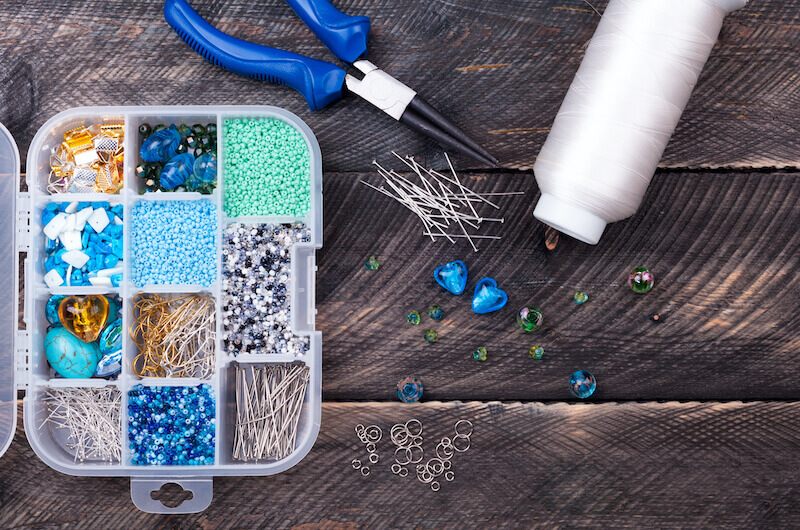 nożyczki, nić i koraliki na stole pojemnik z niebieskimi koralikami