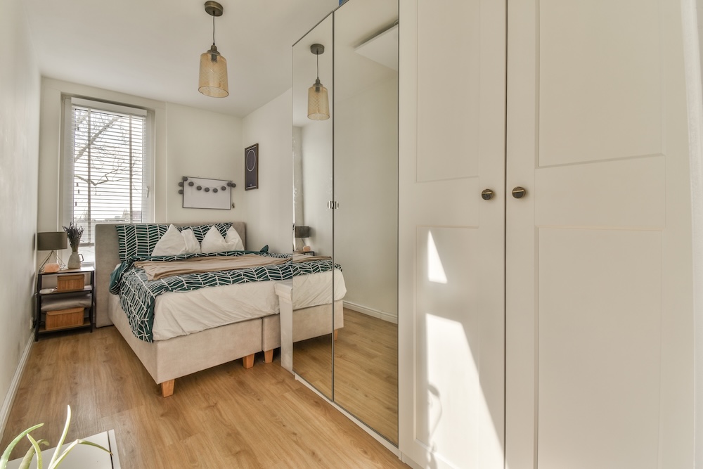 pokój z białą szafą i łóżkiem pod oknem  mały pokój z wąskim przejściem i meblami pod ścianą