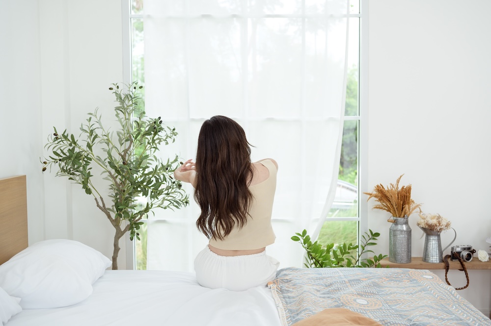 okno w sypialni z pojedynczą firanką w białym kolorze  okno w sypialni z łóżkiem i drzewkiem w rogu