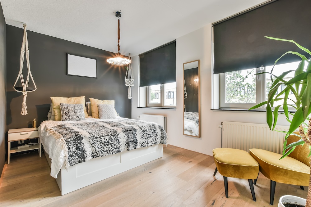 okno w sypialni z szarą ścianą i białym łóżkiem  okno w sypialni zasłonięte roletami w szarym kolorze
