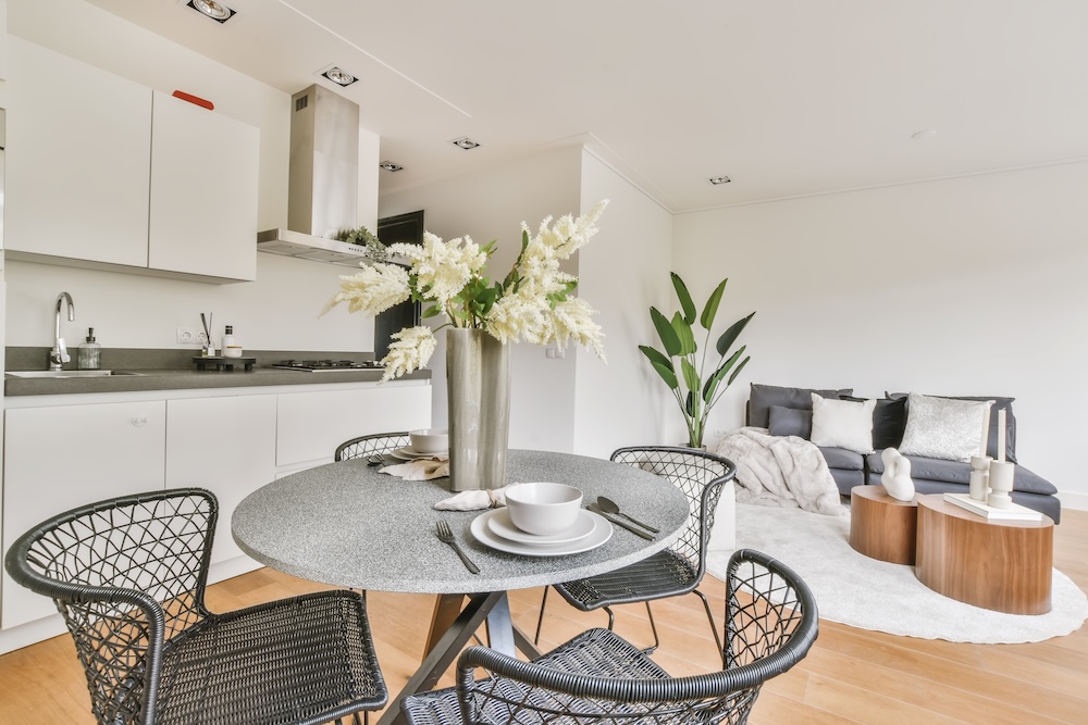 okrągły stół z czterema krzesłami obok białego aneksu kuchennego  mieszkanie z aneksem kuchennym i stołem z krzesłami w szarym kolorze