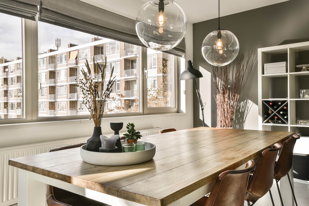 stół z blatem z drewna i białymi nogami pod długim prostokątnym oknem  stół jadalniany z krzesłami pod oknem z widokiem na blok